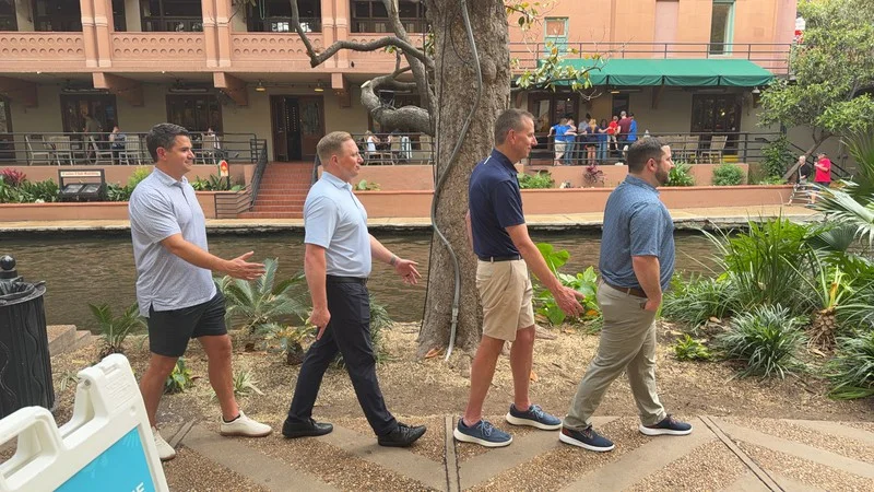 Ally teammates recreate a walking pose outdoors beside the San Antonio River Walk.